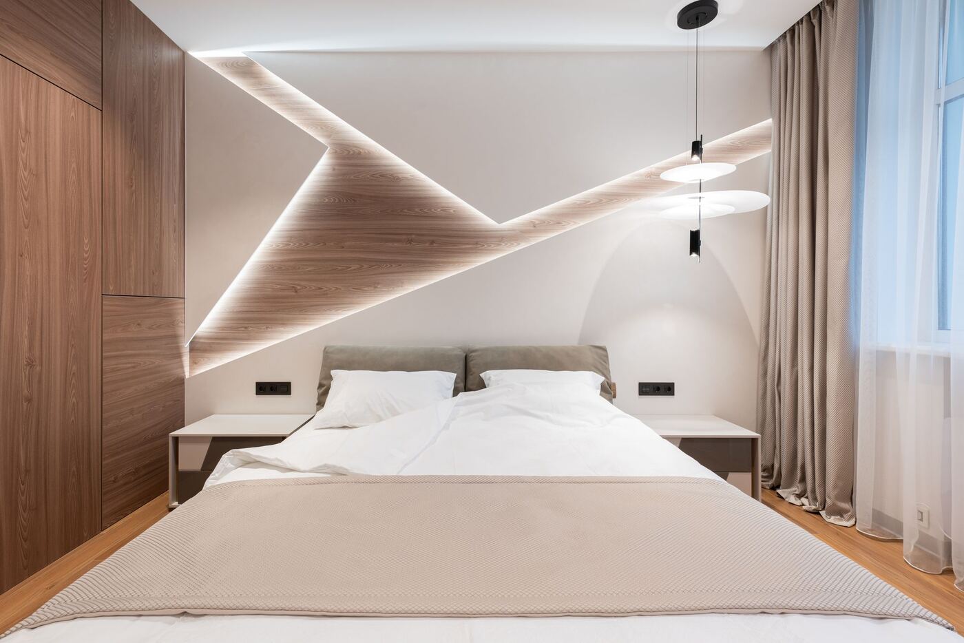 Dormitorio de un apartamento con cama doble, cabecero de madera iluminado y cortinas de lino